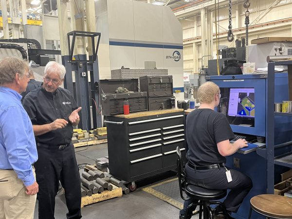 Richard Janik with Cavalier Career Ready participant Cameron. Janik is speaking with Cameron's trainer while Cameron operates a CNC Machine.